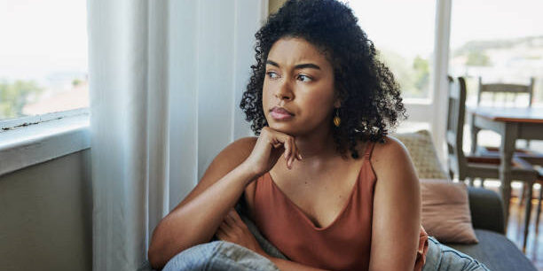 Shot of a young woman looking pensively out a window at home